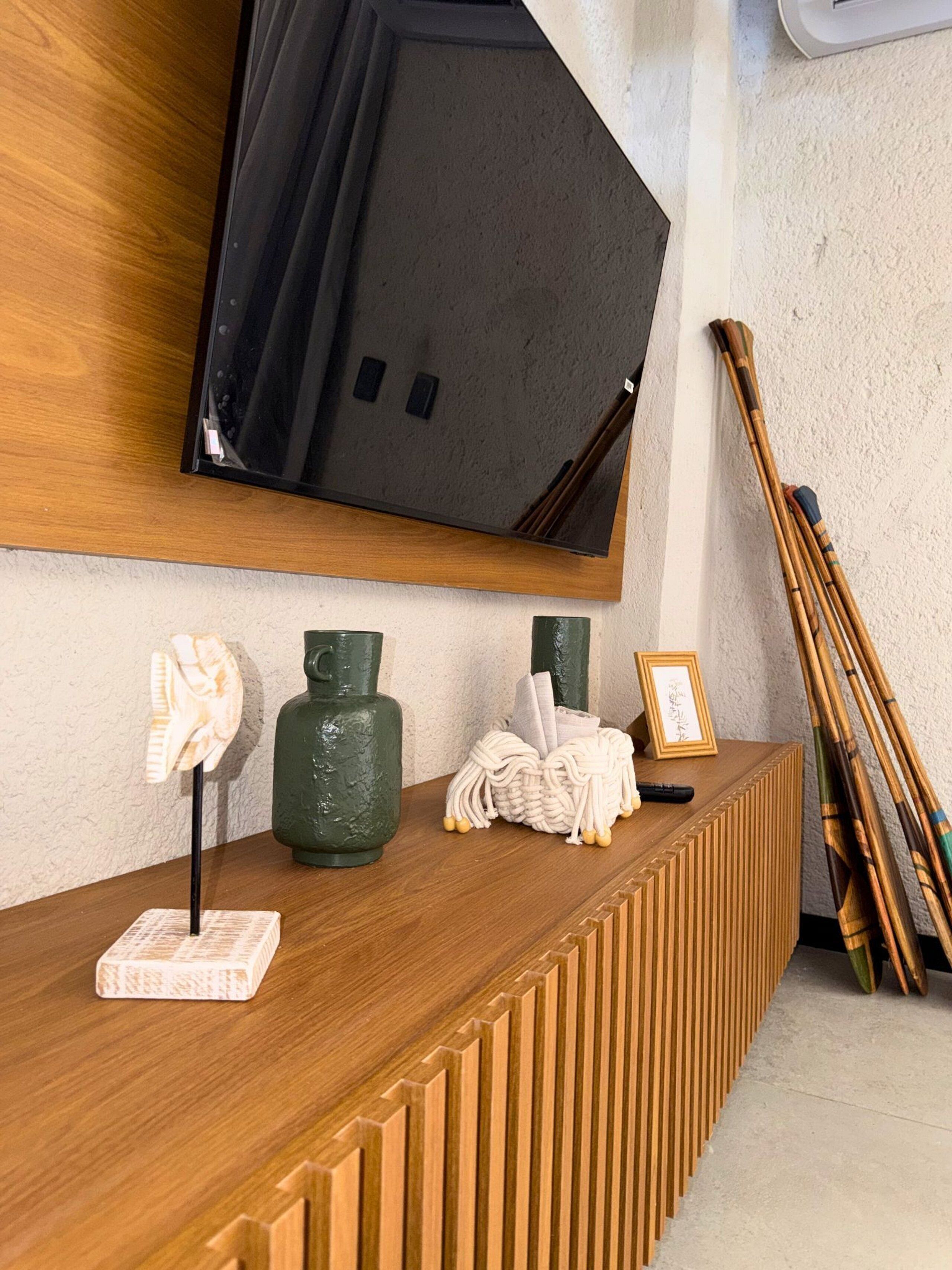 A wooden reception desk with a mounted TV, a framed picture, and a pair of traditional bamboo fans.