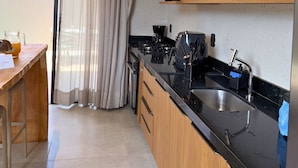 A modern kitchen with a black countertop, wooden cabinets, a stainless steel sink, and a blue appliance on the wall. - MHV Milagres - Nani Villas Boutique (São Miguel dos Milagres)