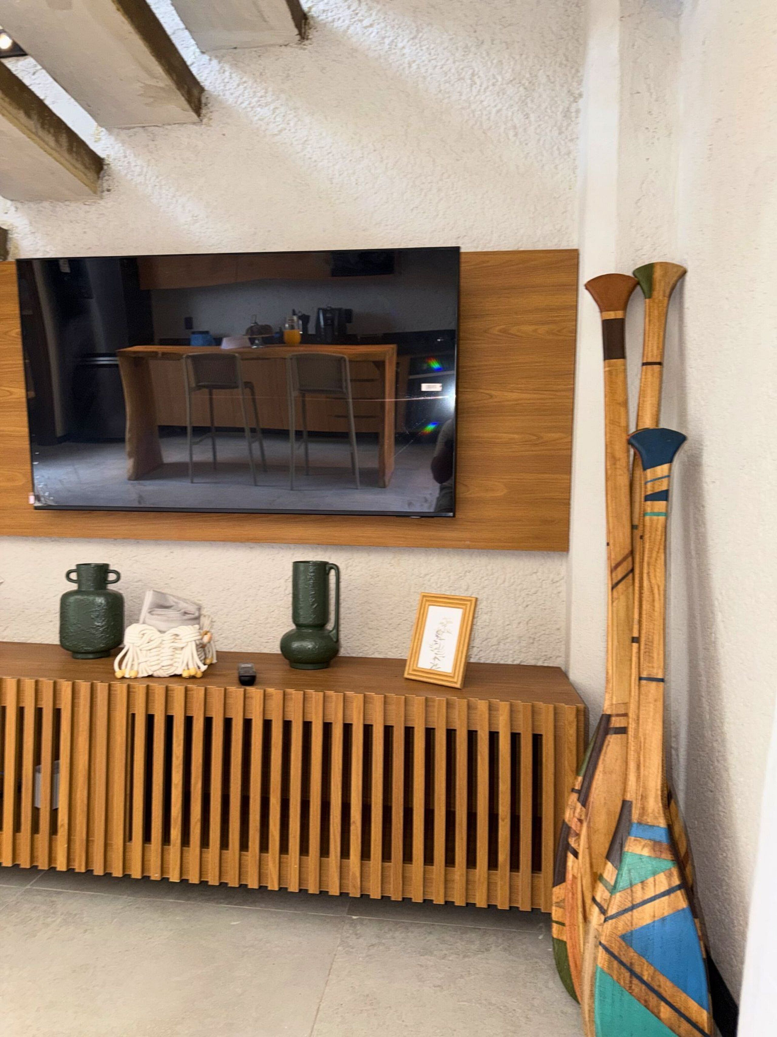 Ein modernes Wohnzimmer mit einem Holzkonsolentisch, einem darüber montierten Fernseher und einem traditionellen japanischen Instrument, das an der Wand lehnt.