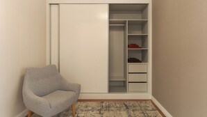 Ein Zimmer mit grauem Sessel, einem weißen Schrank mit mehreren Ablagen und einem gemusterten Teppich.