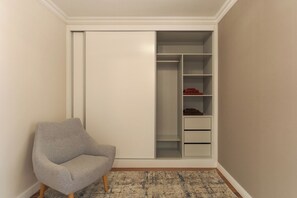 A room with a grey armchair, a white closet with multiple shelves, and a patterned rug. - Stay In Avenue Arriaga 10, by Pausa H. Rentals (Funchal)