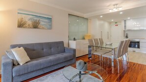 Ein modernes Wohnzimmer mit einem grauen Sofa, einem Glastisch und einem Essbereich mit einem Tisch und Stühlen.