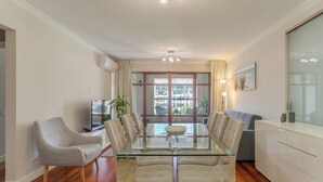 Ein modernes Wohnzimmer mit einem Glastisch, beigen Sofas und einem Fernseher auf einem Lowboard.