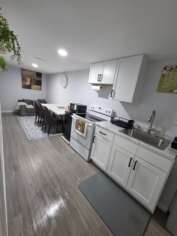 Cocina moderna con armarios blancos, microondas, estufa y lavamanos. Hay un comedor con mesa y sillas.
