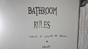 Een badkamermuur met de tekst 'BATHROOM RULES' en een handdesinfecteerder.