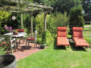 Eine Terrasse mit Tisch, Stühlen, einer Pergola und zwei Liegestühlen.