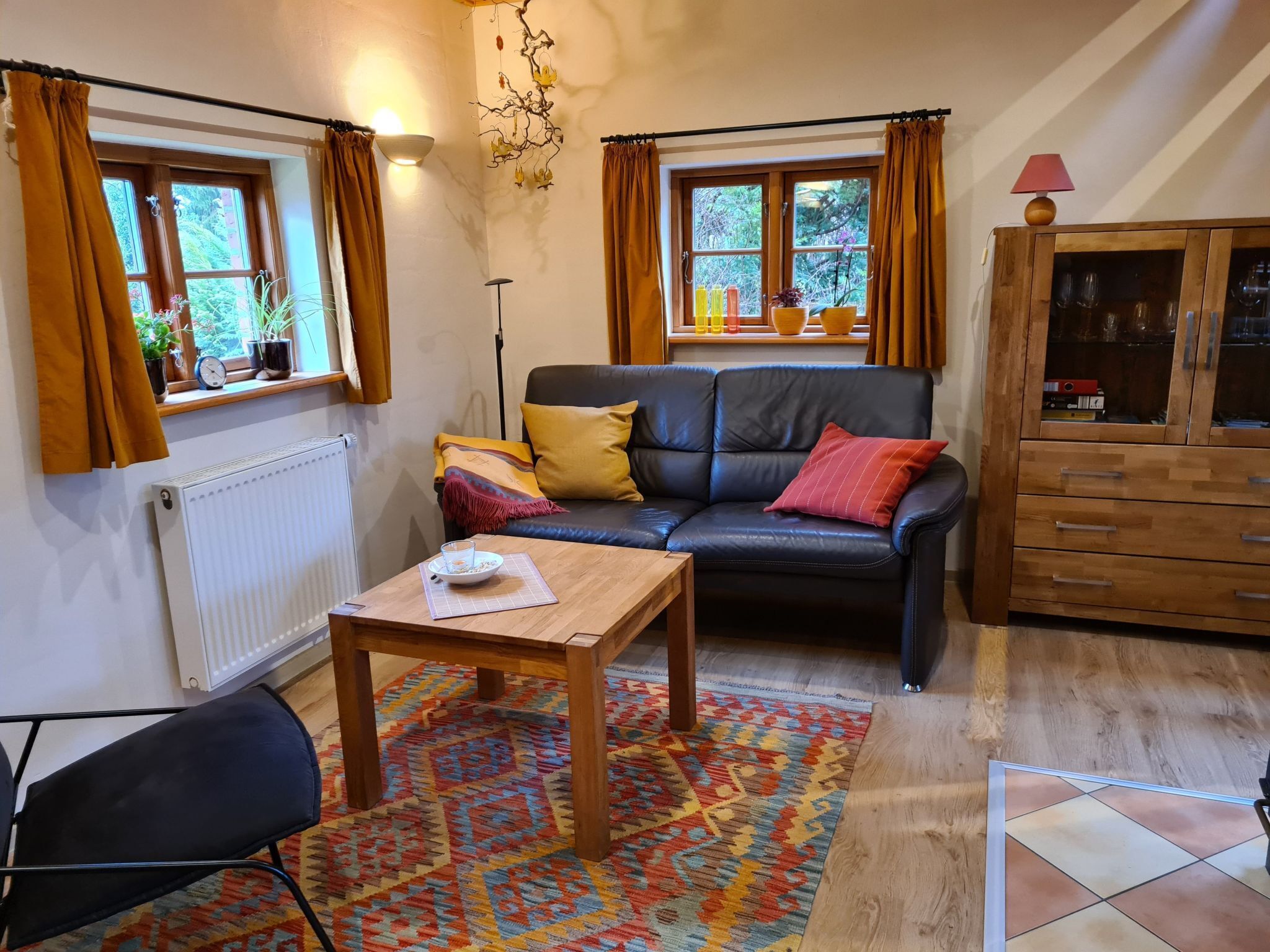 A cozy living room with a black leather sofa, a wooden coffee table, and a patterned rug.