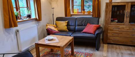 A cozy living room with a black leather sofa, a wooden coffee table, and a patterned rug.