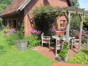 Ein Backsteinhaus mit einer Holzpergola, einem Tisch mit Stühlen und einem Blumentopf.