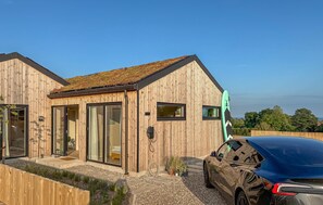 Ein modernes Holzhaus mit großen Fenstern, ein Auto davor und ein klarer Himmel.