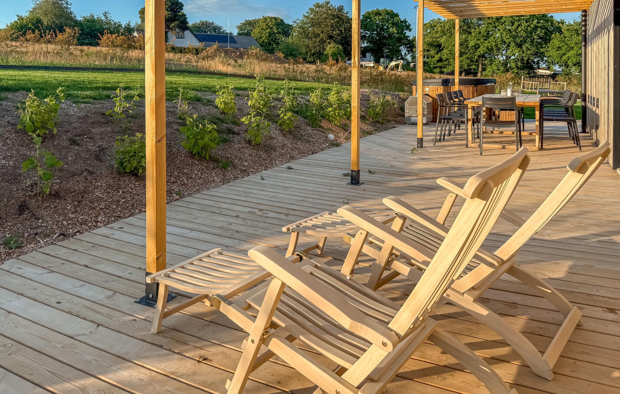 Une terrasse en bois avec des chaises longues, un espace barbecue et une vue sur un champ.