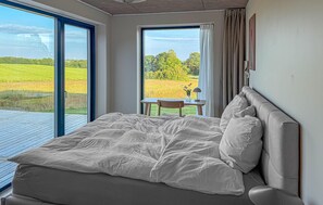 A bedroom with a large bed, a small table with a chair, and a view of a green field through a window. - 4 bedroom beautiful home in Haderslev (Haderslev)