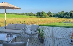 A deck with outdoor furniture, a large umbrella, and a view of a green field. - 4 bedroom beautiful home in Haderslev (Haderslev)