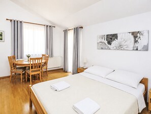 Une chambre d’hôtel avec un lit, une table à manger avec des chaises, un tableau au mur et une fenêtre avec des rideaux.