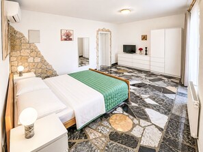 A bedroom with a bed, a dresser, a television, and a stone wall. - Ein Apartment im Ferienhaus Zweirosen by Interhome (Fažana)