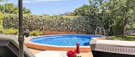 A poolside area with lounge chairs, a table with a bottle and glasses, and a view of a swimming pool.