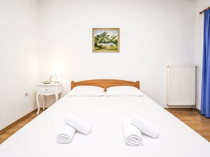 Ein Hotelzimmer mit einem hölzernen Bett, weißen Leinen, einem Nachttisch mit Lampe, einem Bild an der Wand und einer Heizung.