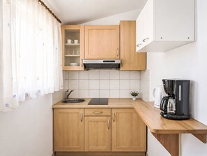 Eine Küche mit Holzschränken, einer Edelstahlspüle, einer schwarzen Kaffeemaschine und einem kleinen Topfpflanzen.