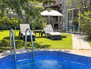 Piscina com borda azulejada, cercada por um gramado e espreguiçadeiras.