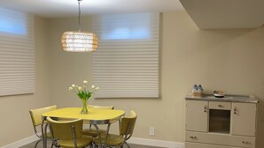 Een eetgedeelte met een ronde tafel en stoelen, een hanglamp en een kitchenette met kastjes.