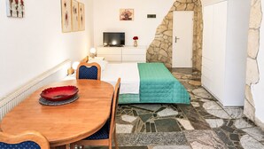 A compact room with a bed, a television, a dining table, and a stone wall. - Ein Apartment im Ferienhaus Zweirosen by Interhome (Fažana)