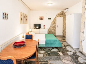 A compact room with a bed, a television, a dining table, and a stone wall. - Ein Apartment im Ferienhaus Zweirosen by Interhome (Fažana)