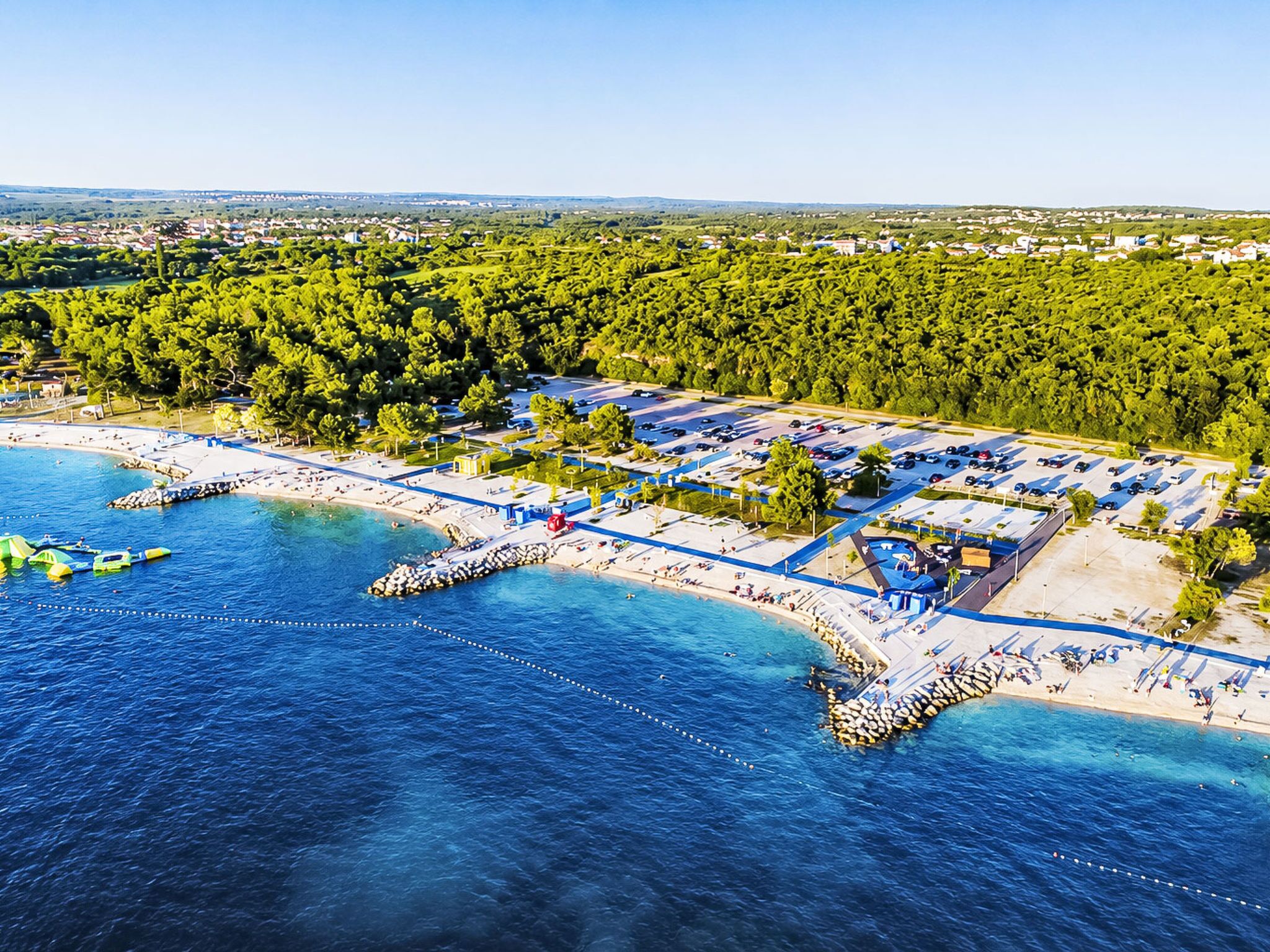 Eine Luftaufnahme einer Küstenregion mit einem Hafen, Strand und umliegendem Wald.