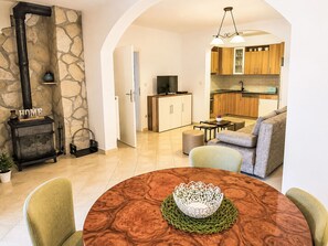 A modern living room with a fireplace, a dining table with a decorative centerpiece, and a kitchen area with wooden cabinets and a television. - Ein Apartment im Ferienhaus Zweirosen by Interhome (Fažana)