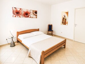 A bedroom with a wooden bed, a chair, and two wall-mounted artworks. - Ein Apartment im Ferienhaus Zweirosen by Interhome (Fažana)