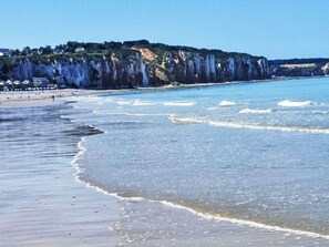 Una playa con agua cristalina, una orilla arenosa y acantilados al fondo.