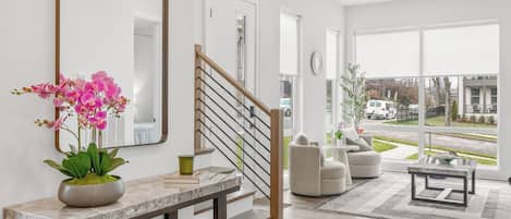A modern interior with a staircase, a large mirror, a potted orchid, and a view of the outside.