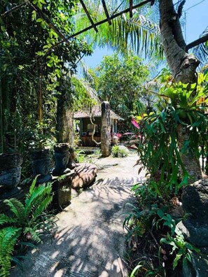 Um jardim tropical com um caminho de pedra, vegetação exuberante e uma pequena estrutura semelhante a uma cabana.