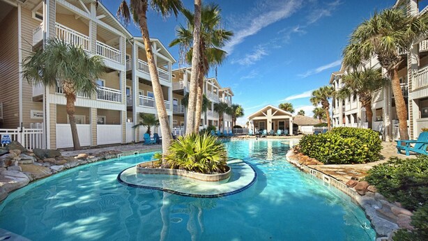 A swimming pool surrounded by palm trees and a building with balconies. - 3 Bedroom Townhome-Resort Style Pool (Corpus Christi)