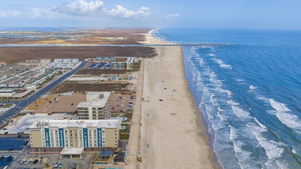 An aerial view of a coastal area with a beach, a hotel, and a road. - Y Knot Go to the Beach! Cute Beach Condo (Corpus Christi)