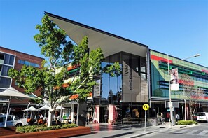 A modern building with a glass facade, a covered entrance, and a sign indicating a business center. - KozyGuru | Box Hill | New Designer Home (Box Hill)