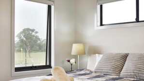 Une chambre à coucher avec un lit, deux fenêtres, une lampe et un vase rempli de fleurs.