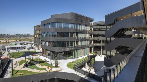 Un bâtiment moderne à plusieurs étages, doté d’une façade incurvée, de grandes fenêtres et d’une cour intérieure aménagée avec des espaces pour s’asseoir et de la verdure.