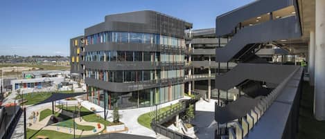 A modern multi-story building with a curved facade, large windows, and a central courtyard with seating and greenery.