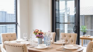 Une table à manger dressée pour quatre personnes, avec des chaises, un vase de fleurs et des bouteilles d’eau.
