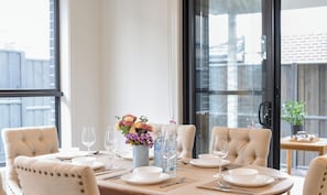 Une table à manger dressée pour quatre personnes, avec des chaises, un vase de fleurs et des bouteilles d’eau.