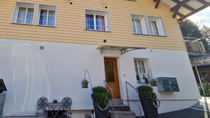 En toetagers bygning med gul facade, hvide detaljer og en overdækket veranda med udendørs siddepladser.