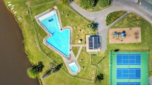 Ett flygbildsbild av ett semesterområde med en swimmingpool, tennisbanor och en vattenpump som drivs med solenergi.