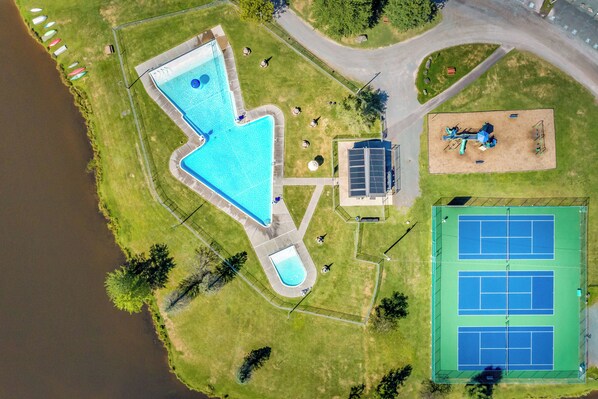 An aerial view of a resort with a swimming pool, tennis courts, and a solar-powered water pump.