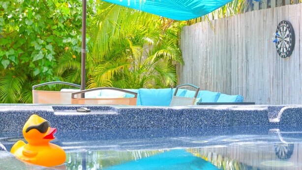A pool area with a rubber duck, a blue umbrella, and a dartboard on the wall. - The HotTub Hideaway-5 Min From Sombrero Beach (Marathon)