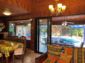 A dining area with a pool view, brick walls, and a ceiling fan.
