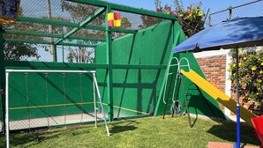 Une aire de jeux clôturée avec un toboggan, une balançoire et un petit drapeau.
