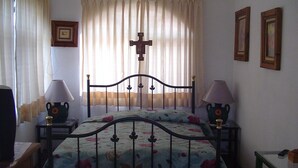 Une chambre à coucher avec un lit, deux lampes de chevet, une croix au mur et des rideaux.