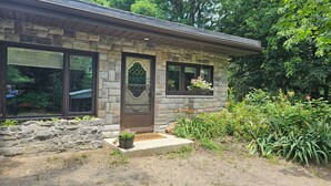 A stone house with a front door, two windows, and a small porch area with a potted plant. - Total Tranquility Apartment in a country setting. Pet friendly (Brant)
