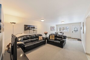 A living room with a black leather sofa, a flat-screen TV, and a floor lamp.