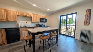 A kitchen with wooden cabinets, a central island with stools, a dishwasher, and a large window with a view. - Village Overlook: Spacious 5 BR + Prime Location (Lake George)